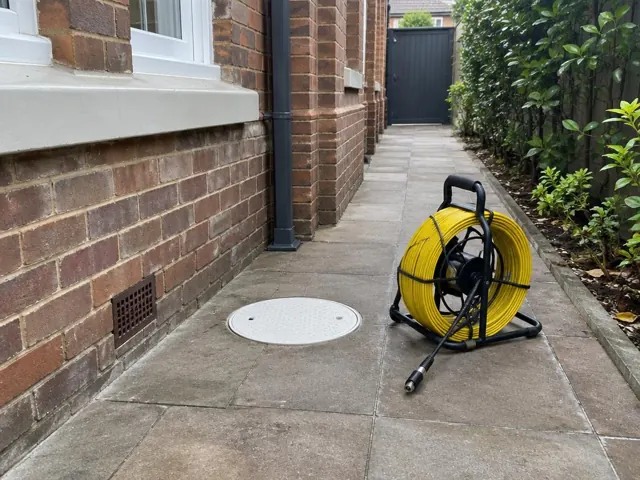 Capped inspection opening and drain camera reel on a paved side path beside a brick house in Bellevue Hill