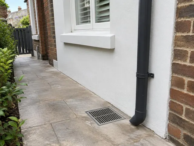 Outdoor grated gully beside a white rendered wall and brick house in Edgecliff