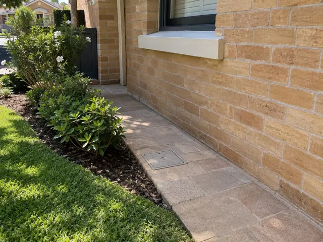 Flush square access cover in paved side path beside brick house and garden in Double Bay