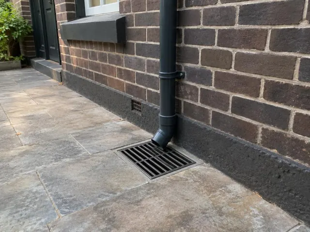Cleared stormwater grate beside a brick house wall and tiled paving in Double Bay